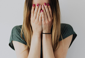 Mujer cubriendo su rostro con las manos, mostrando una expresión de tristeza o preocupación.
