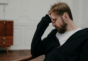 Hombre sentado en una silla con la cabeza entre las manos, mostrando una expresión de angustia o preocupación.