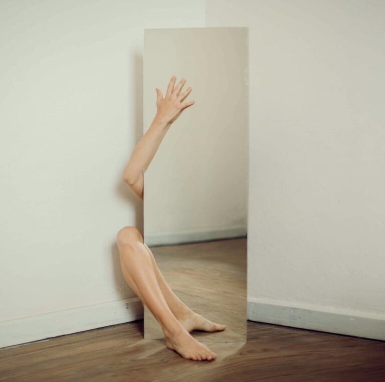 Persona sentada en el suelo con las piernas extendidas frente a un espejo.